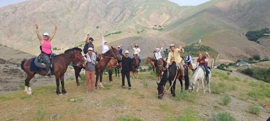 A group of riders and horses gathered on grass in a mountain valley