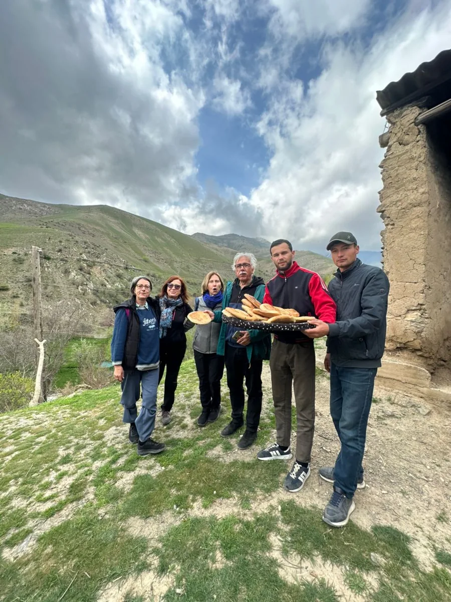 Travelers gathered beside a traditional building with green hills behind them