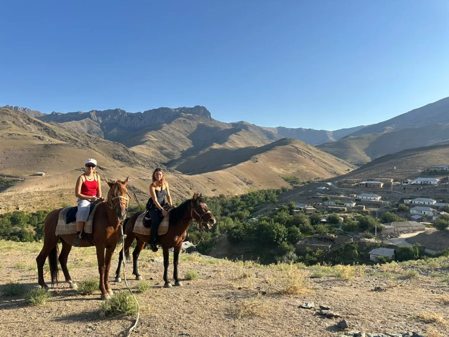 Two travelers on horseback overlooking a sunlit mountain village