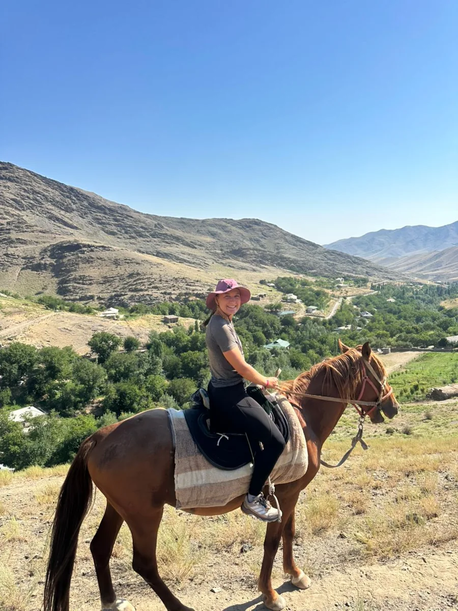 A traveler on horseback on a mountain path above a green village