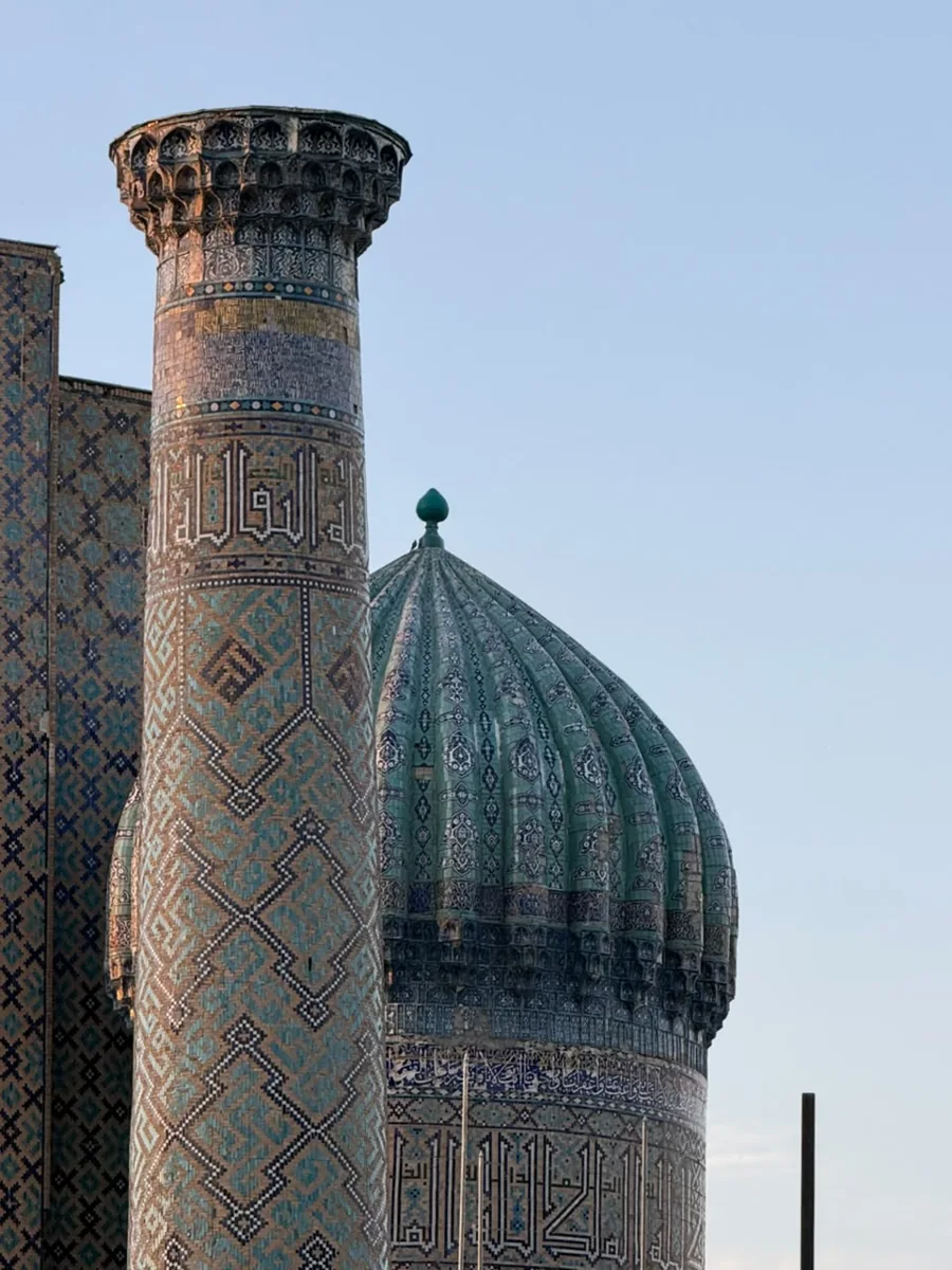 Intricate blue tilework on a minaret beside a ribbed turquoise dome in Samarkand