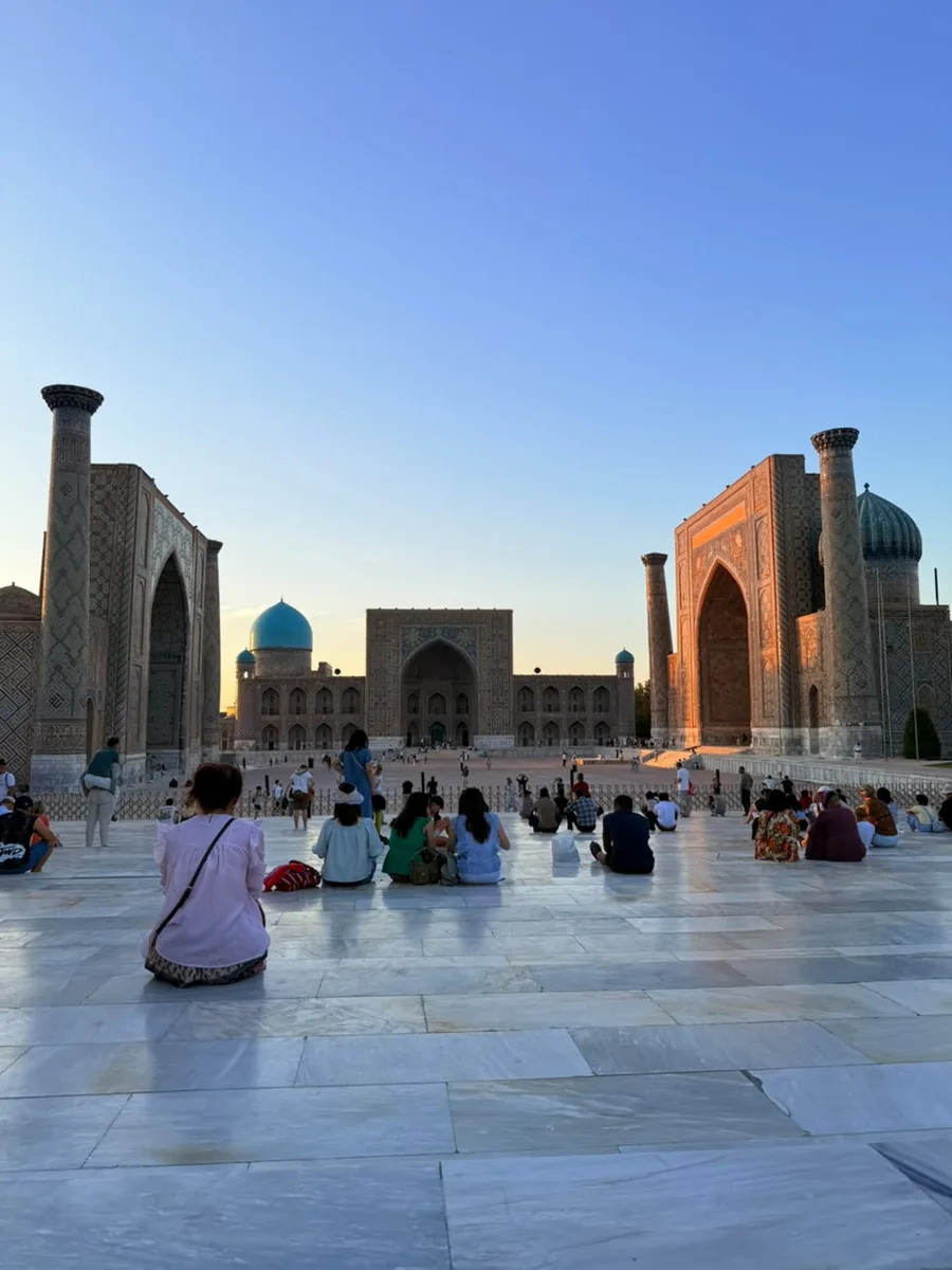 Visitors sitting in Samarkand Registan Square beneath a clear evening sky