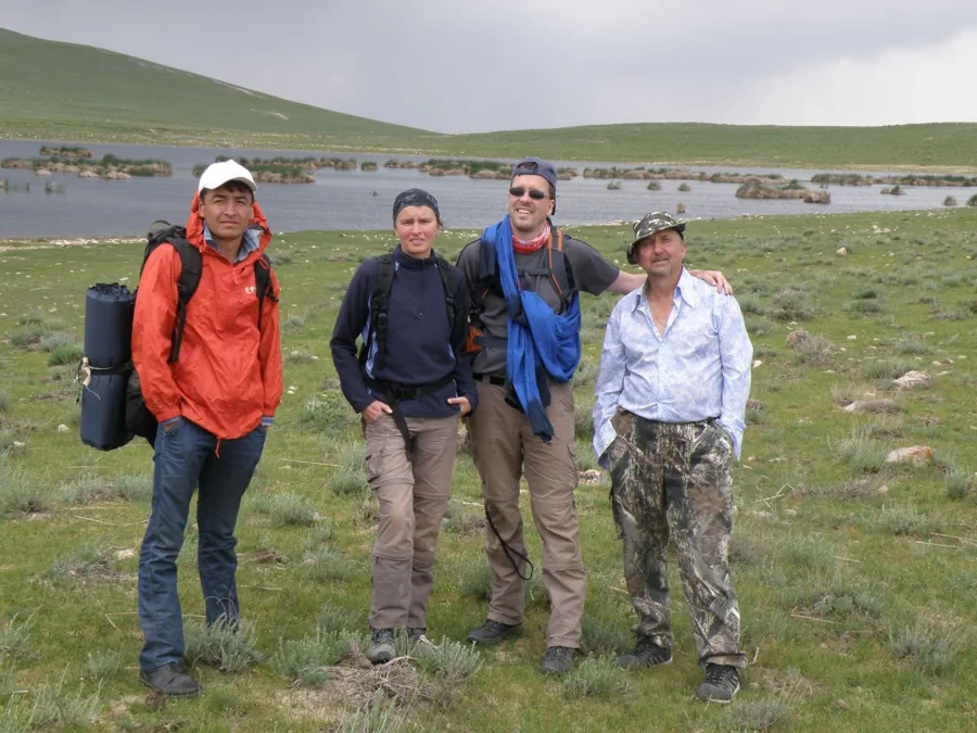 Four travelers standing in grass near a lake with hills behind them