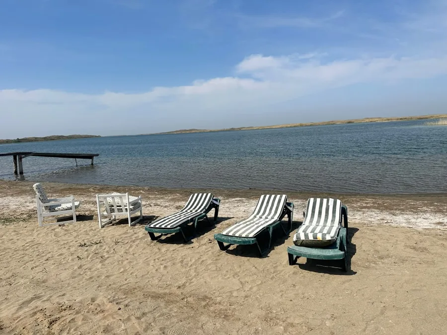 Striped loungers on a sandy lakeshore beside calm blue water