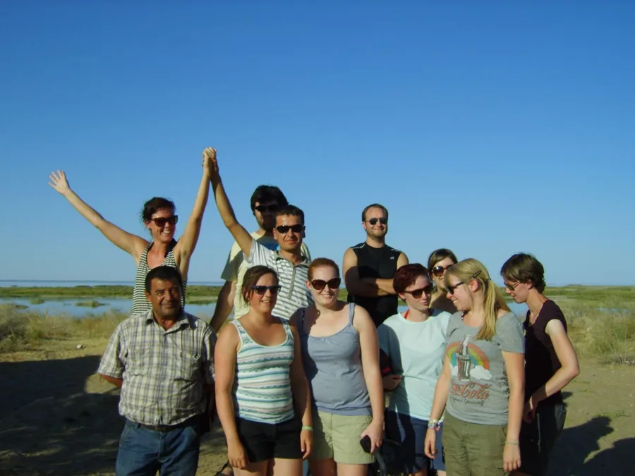 Travelers posing together beside a lake under a bright blue sky