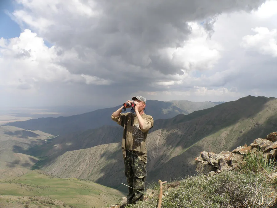 A hiker looking through binoculars from a rocky mountain viewpoint