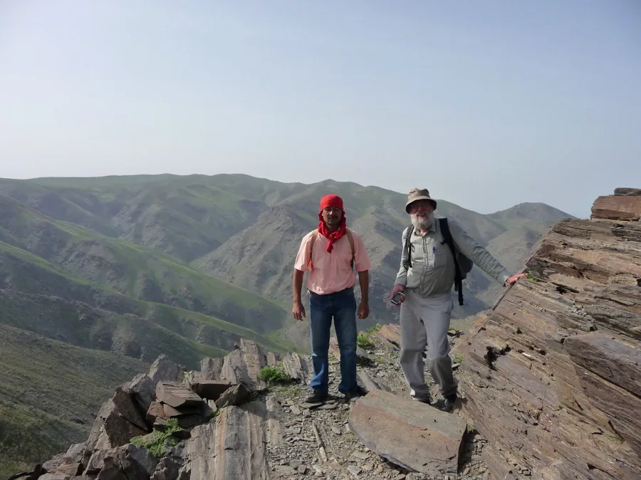 Two hikers walking on a rocky ridge with layered mountains behind them
