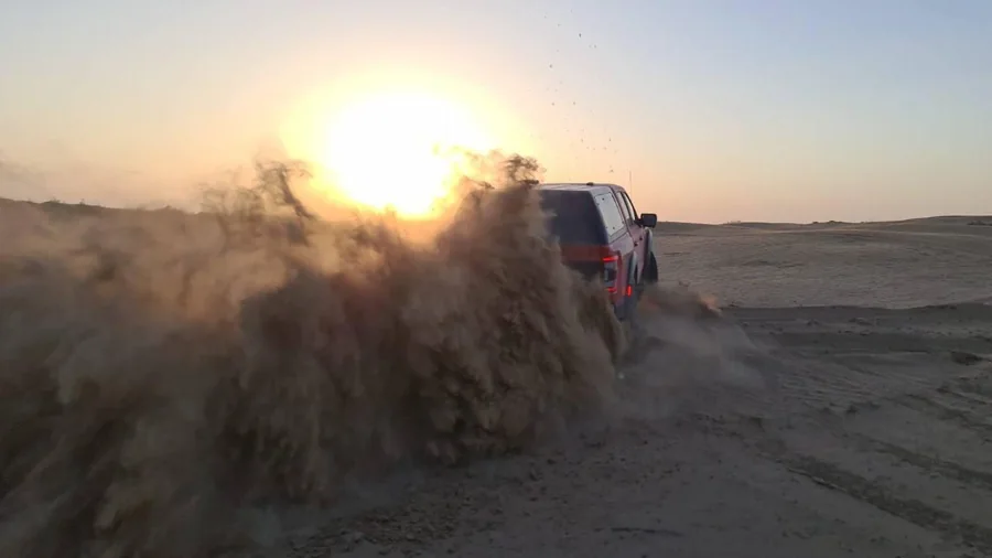An off-road vehicle crossing sand with dust glowing in the setting sun