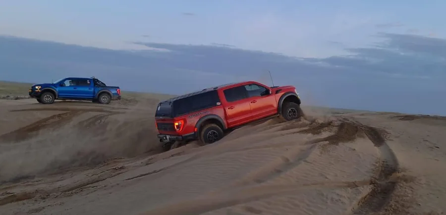 Off-road vehicles resting on sandy dunes under a blue sky
