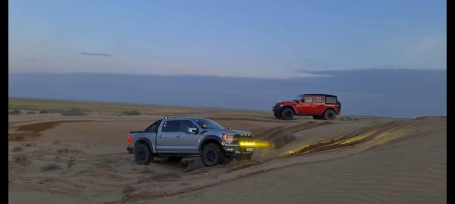Two off-road vehicles crossing a broad sandy landscape