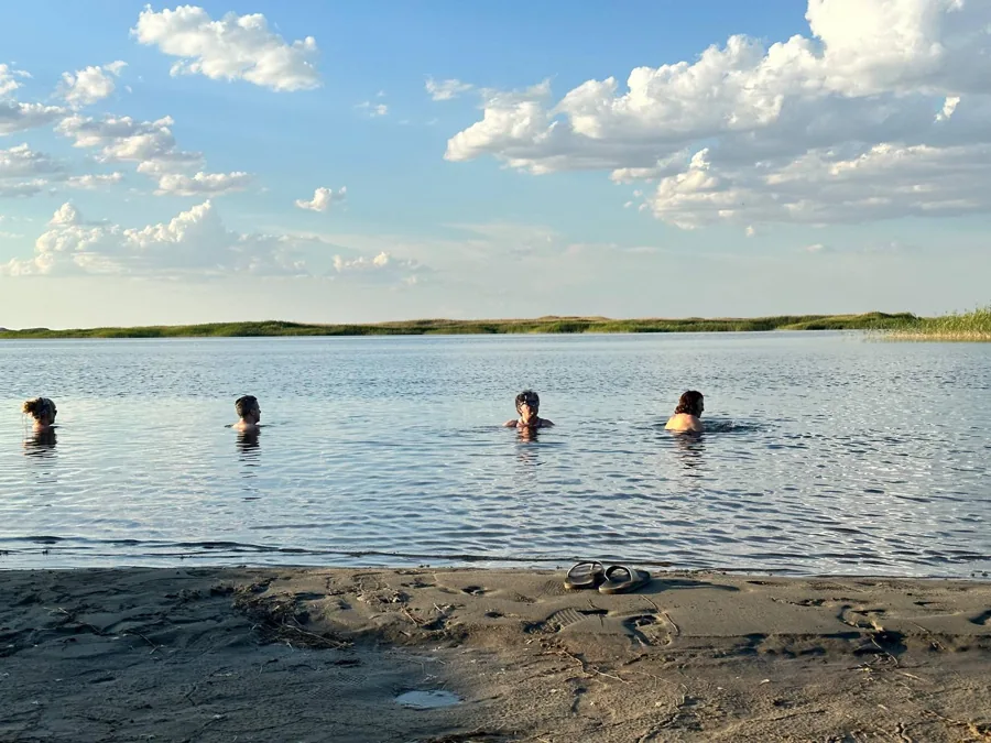 Travelers swimming in a calm lake beneath scattered white clouds