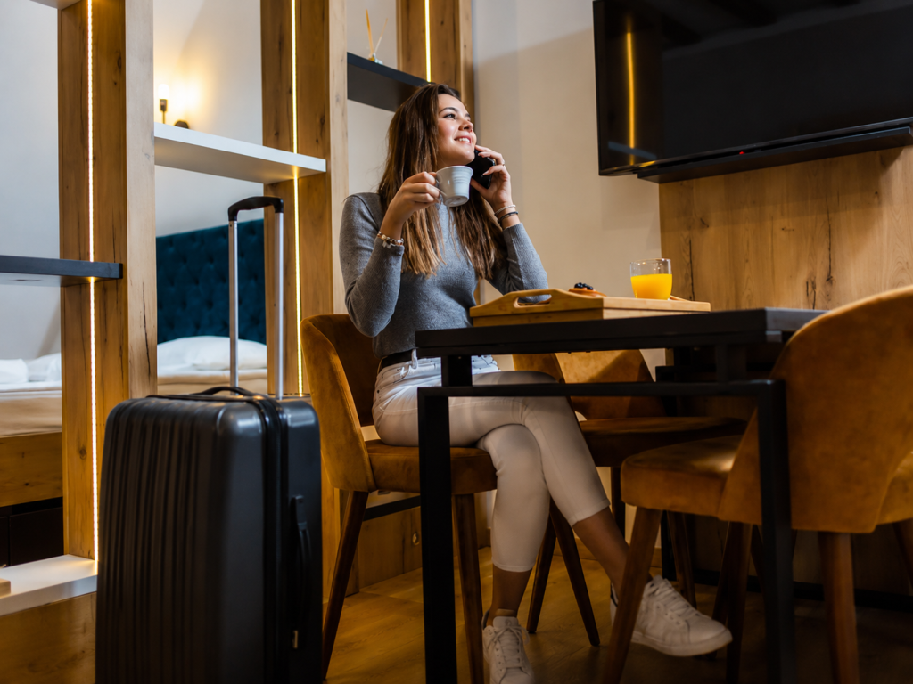 1624b82a-746b-4f9c-bc2c-bfd2dee87e25 - Silk Road Elite - Silk Road Elite Businesswoman using a smartphone beside a laptop in a hotel room