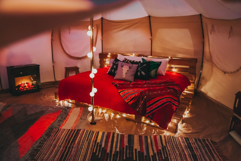 Warmly lit tent interior with a red bed and woven rugs