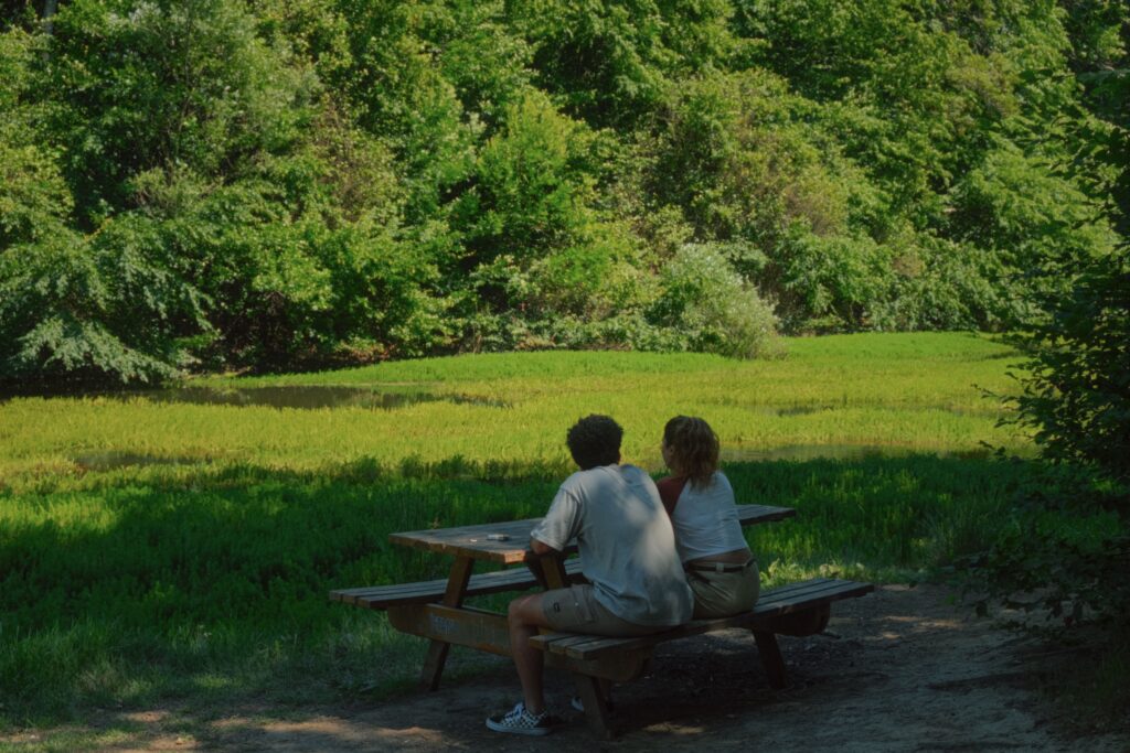 Two travelers resting at a picnic table in a green forest clearing