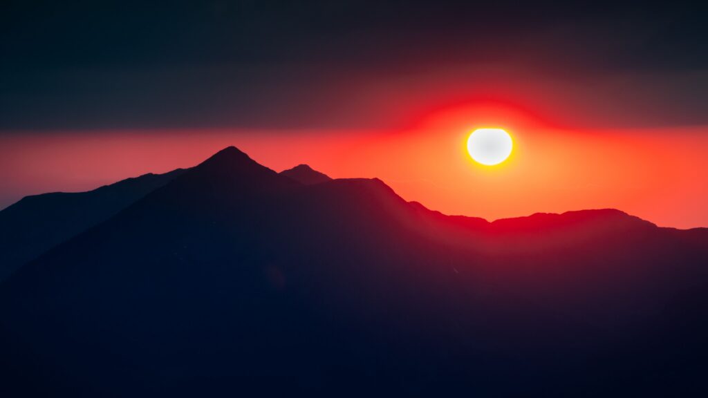 Sun setting behind a dark mountain ridgeline