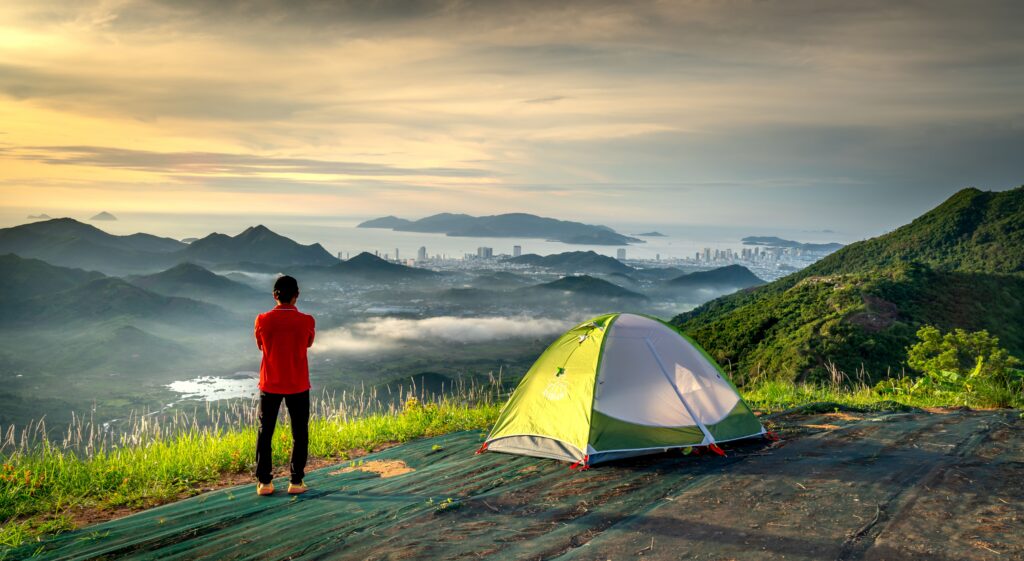Camper standing beside a tent above a misty mountain valley