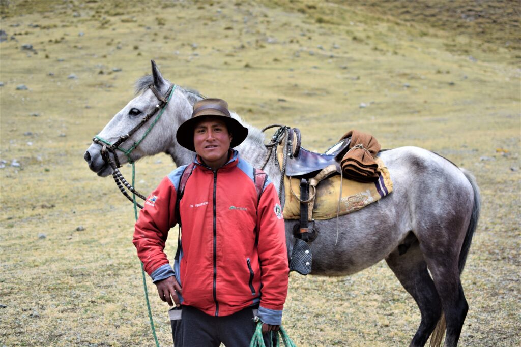 Riding guide standing beside a saddled gray horse