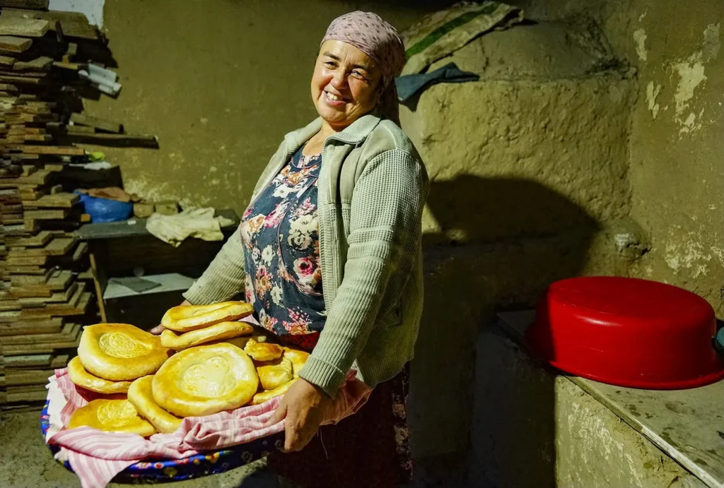 Village baker holding freshly baked round loaves beside a clay oven