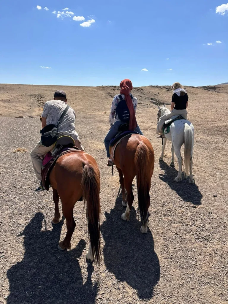 Three riders seen from behind cross open rocky ground under a blue sky