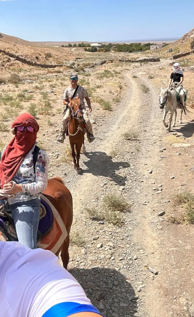 Horse riders follow a rocky track through an arid valley near a village