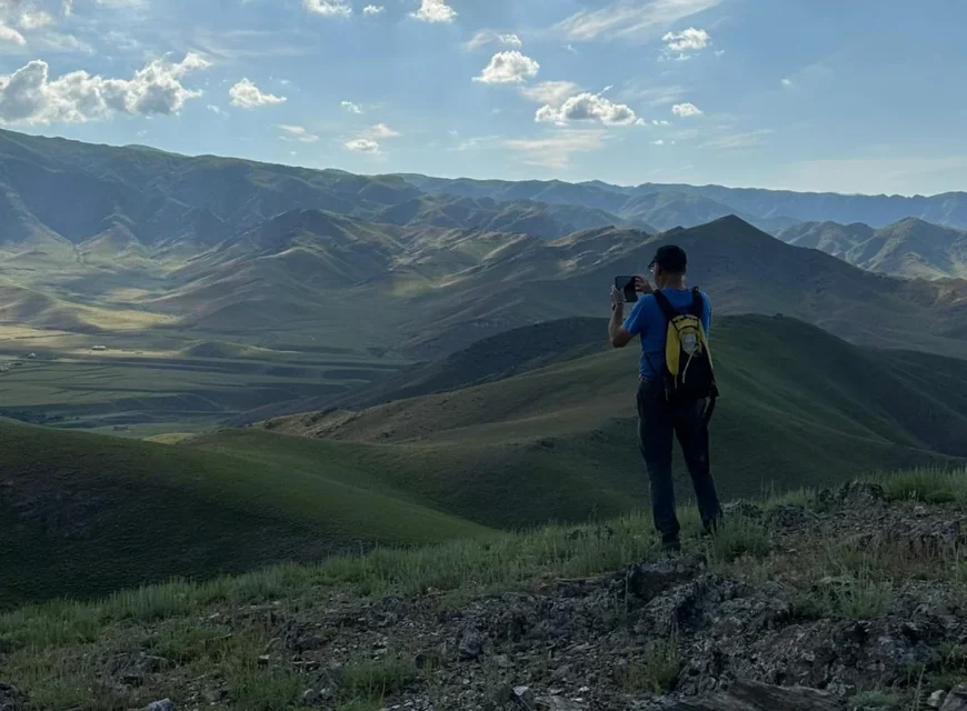Hiker photographing a panoramic view of the Nuratau Mountains