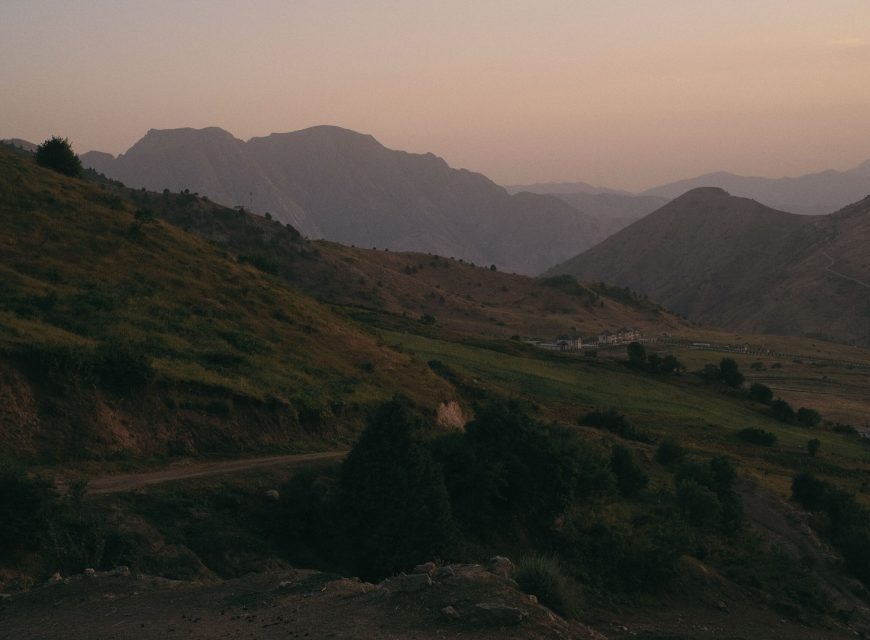 Hazy dusk landscape view of shadowy mountain layers and rolling green hills at sunset in Central Asia.