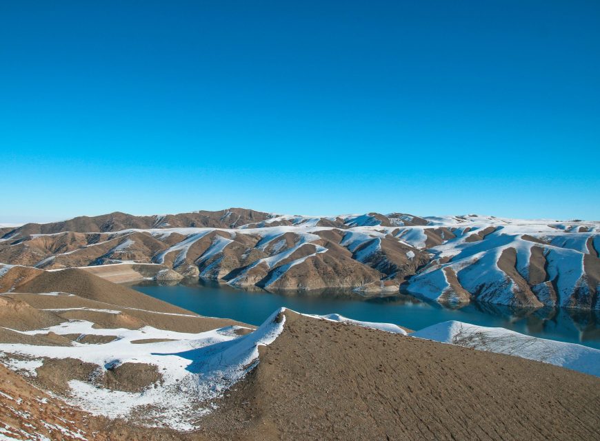 Barren hills with patches of snow under a blue sky